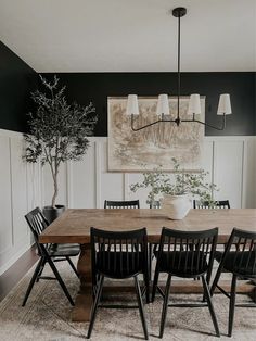 a dining room table and chairs in front of a black wall with white paneling