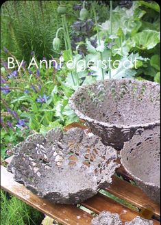 three stone bowls sitting on top of a wooden bench in front of plants and flowers