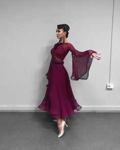 a woman in a purple dress is standing against a wall with her arms spread out