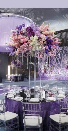 an elegant wedding setup with purple and white flowers in tall centerpieces at the head table