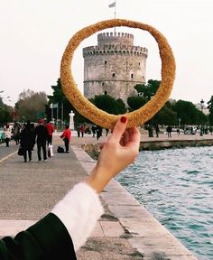 a person holding up a doughnut in front of a body of water with a castle in the background