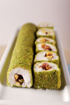 there is a green roll with white icing and nuts on the top it sits on a plate