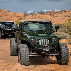 two green jeeps driving down a dirt road