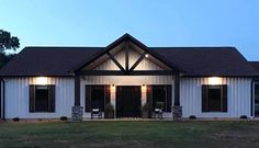 a white house with black shutters and lights on it's front door is lit up at night