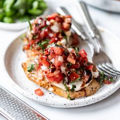 a white plate topped with bruschetta chicken covered in tomatoes and onions next to a fork