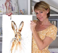 a woman holding up a painting of a rabbit