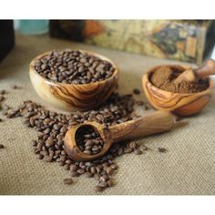 two wooden bowls filled with coffee beans next to a scoop of ground coffee on a table