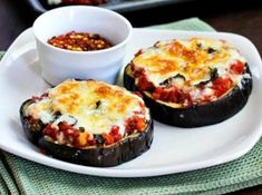 two stuffed eggplant halves on a white plate with a small bowl of chili