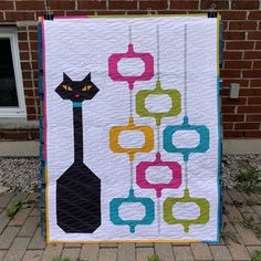 a black cat sitting on top of a quilt next to a brick wall and grass