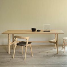 a wooden table with two chairs and a laptop on top of it in front of a white wall