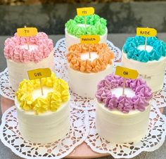 there are four cakes with different colored frosting on the cake plate and one has a name tag