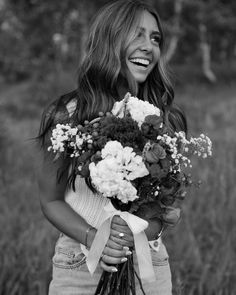 a woman holding a bouquet of flowers in her hands and smiling at the camera while standing in a field