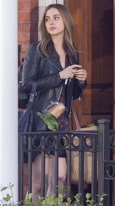 a woman in black jacket and skirt standing on balcony next to door with handbag