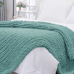 a bed with a green blanket on top of it next to a white comforter