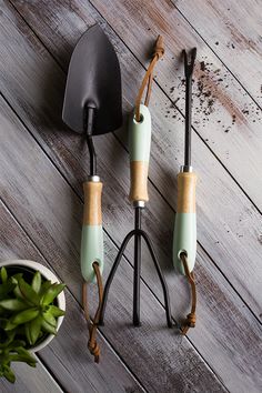 three garden tools sitting on top of a wooden floor next to a potted plant