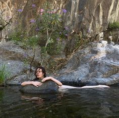 a woman laying on top of a large rock in the water next to a waterfall