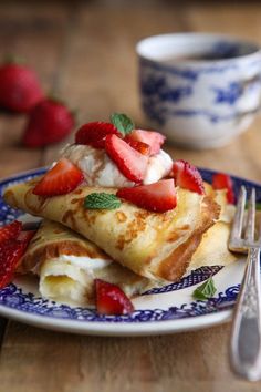 a plate topped with crepes and strawberries next to a cup of coffee