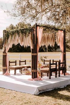 an outdoor wedding set up with pink drapes and wooden benches for the guests to sit on