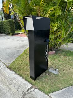 a tall black box sitting on the side of a road next to a palm tree