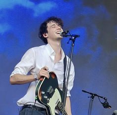 a man singing into a microphone and holding a guitar in front of him on stage