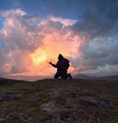 a person sitting on top of a hill with their arms outstretched as the sun sets