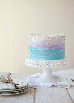 there is a cake with blue, pink and white frosting on it next to plates