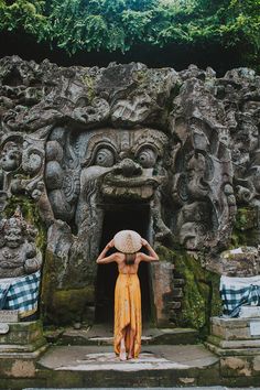 a woman in a yellow dress and hat standing by an entrance to a stone structure