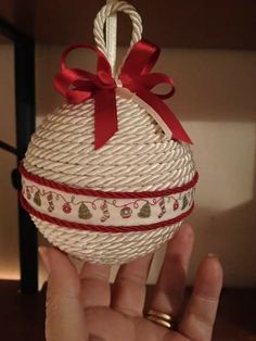 a hand holding a white and red christmas ornament with ribbon on the top