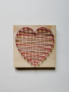 a heart shaped string art piece on a wooden plaque with red and white strings attached to it