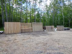 several wooden fences in the middle of a dirt lot with trees behind them and other wood structures