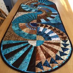 a table top with a blue and brown quilt on it's center piece, sitting on a wooden table