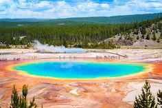 people are standing at the edge of a large pool of colored water in yellowstone national park