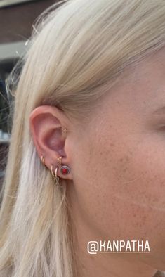 a woman with blonde hair wearing gold ear cuffs and red stone studs on her left ear