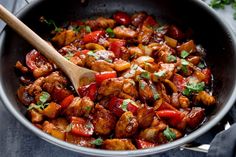 a skillet filled with chicken and vegetables on top of a black table next to a wooden spoon