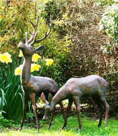 two bronze deer statues standing next to each other in the grass with daffodils behind them