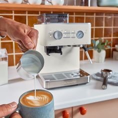 a person pouring something into a cup on top of a counter next to a coffee maker