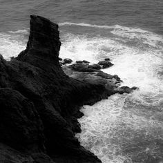 a black and white photo of the ocean with waves coming in from the rocks on the shore