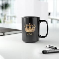 a black coffee mug sitting on top of a white table next to a pen and laptop