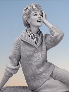 a woman sitting on the ground with her hands to her face and wearing a sweater