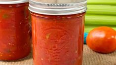 two jars filled with tomato sauce sitting on top of a table next to some vegetables