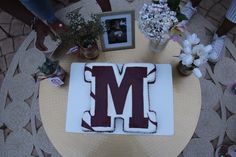 a cake with the letter m on it sitting on top of a table next to flowers