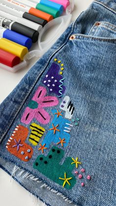 a pair of jean pants with colorful patches on them and markers next to it,