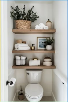 a white toilet sitting in a bathroom next to two shelves filled with towels and plants