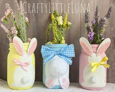 three painted mason jars with bunny ears and flowers in them, one has a bow on its head