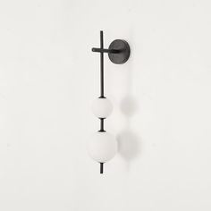 two white balls hanging from the side of a black wall mounted light on a white wall