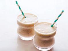 two glasses filled with smoothies sitting on top of a white table next to each other