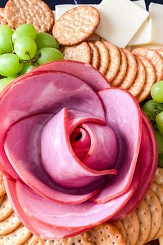 a pink flower surrounded by crackers and grapes on a platter with cheeses