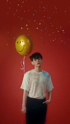 a young man standing in front of a red wall with a smiley face balloon attached to his head