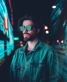 a man wearing green sunglasses standing in front of a wall with neon lights on it