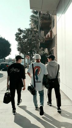 three men walking down the sidewalk with their bags in hand and one man wearing a white t - shirt